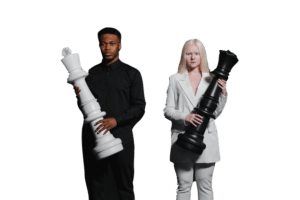 A man dressed in black holds a large white chess king piece while a woman dressed in white holds a large black chess queen piece. They are standing against a plain, neutral background, embodying the essence of strategy and change management.