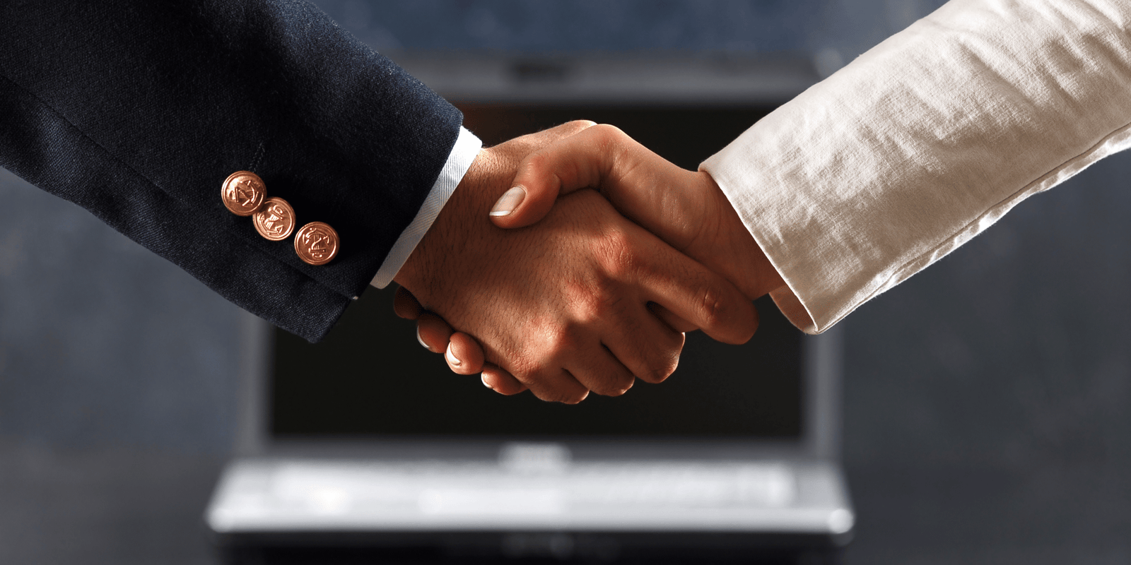 Close-up of two people shaking hands, one in a dark suit with gold buttons and the other in a light-colored outfit. A blurred laptop is visible in the background, suggesting a strategic business or professional agreement focused on results.
