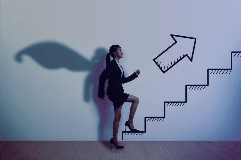 A woman in a business suit and high heels steps up an illustrated staircase on a wall, with a large upward arrow above it. Her shadow forms wings on the wall, symbolizing ambition and progress.