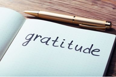 Open notebook with the word "gratitude" in clear letters, inviting a moment of reflection or journaling. A gold pen rests nearby on the wooden table, symbolizing a shared appreciation within the community.